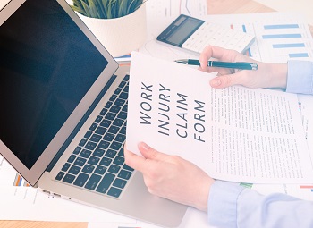 Person holding a work injury claim form in front of a laptop