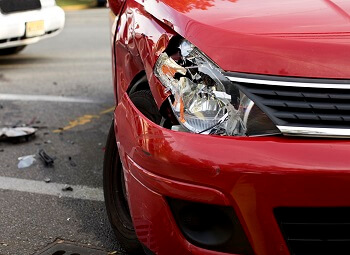 Closeup of a red car with a smashed headlight from a collision with another car